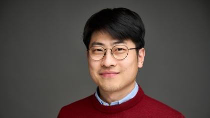 Head shot of an Asian man in his twenties with black hair and wire framed glasses, wearing a blue button down shirt under a burgundy sweater.