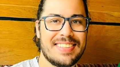 Young white male with black beard and hair, wearing glasses and gray shirt.