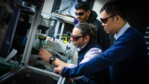 Three males wearing dark goggles working in lab