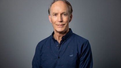 headshot of white man wearing a blue button down patterned shirt
