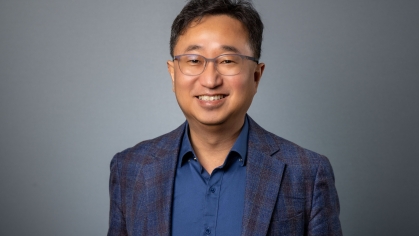 headshot of Asian man with glasses wearng a blue suit and a blue button down shirt