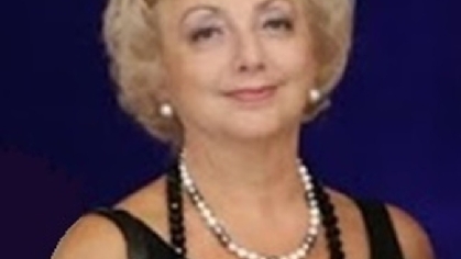 short hair blonde woman wearing white pearl earrings in a black sleevless dress and a black and white long pearl necklace