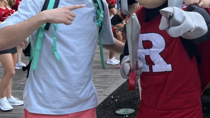 Young man wearing shorts and a T-shirt poses with the Rutgers Scarlet Knight mascot.