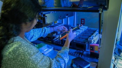 Female student works under lab hood lit with blue light.