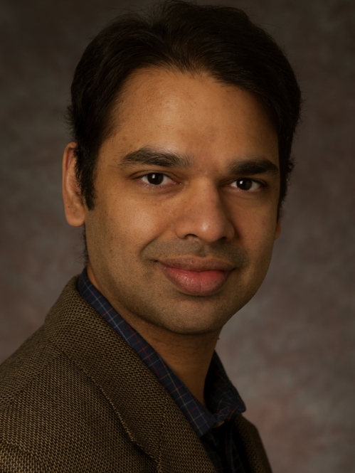 headshot of male with short dark hair wearing a dark brown suit