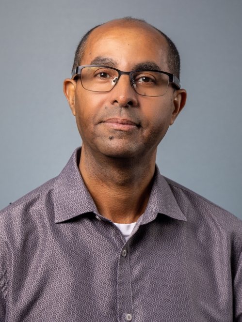 headshot of male with glasses wearing a plum color collared shirt 