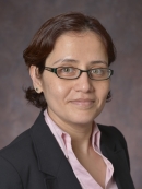 headshot of woman with short brown hair and glasses wearing a dark suit jacket and pink shirtt