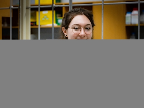 young white woman with brow hair pulled back. She's standing in a lab wearing a lab coat, arms crossed smiling at the camera.