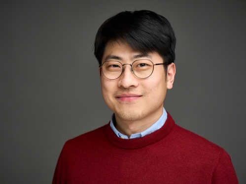 Head shot of an Asian man in his twenties with black hair and wire framed glasses, wearing a blue button down shirt under a burgundy sweater.