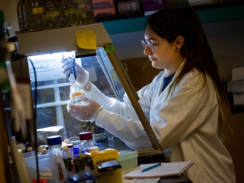 female student with long brown hair and eyeglasses, working in a lab with pipette