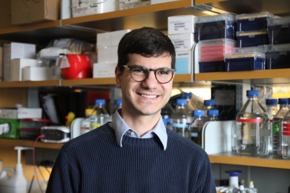 headshot of smiling male with short dark hair and glasses in a lab wearing a sweater and collared shirt