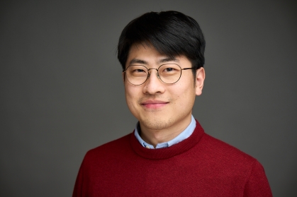 Head shot of an Asian man in his twenties with black hair and wire framed glasses, wearing a blue button down shirt under a burgundy sweater.