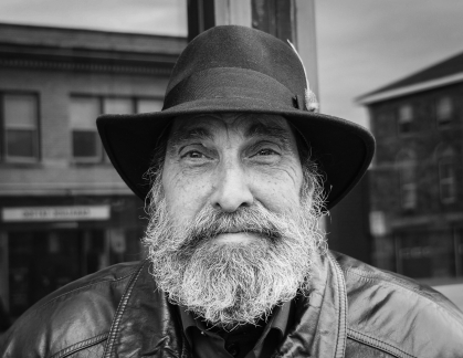 black and white photograph of man with a long beard wearing a black hat and leather jacket