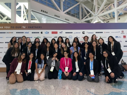 Large group of young women in front of step and repeat banner.