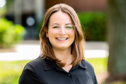 Head shot of female with long brown hair wearing eyeglasses and a black button down shirt.