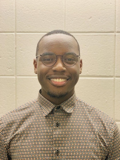 Head shot of Black young man wearing glasses and a light brown collared shirt.