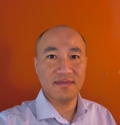 Headshot of an bald man against an orange background wearing a purple shirt.