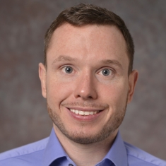 head shot of man with short brown hair wearing a purple button down shirt