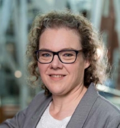head shot of woman with curly light brown hair and eyeglasses wearing a grey suit jacket and white shirt