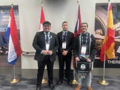 Three young men standing in front of four flags from various countries.