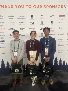 Two male and one female student stand in front of a Thank You to Our Sponsors step and repeat banner.